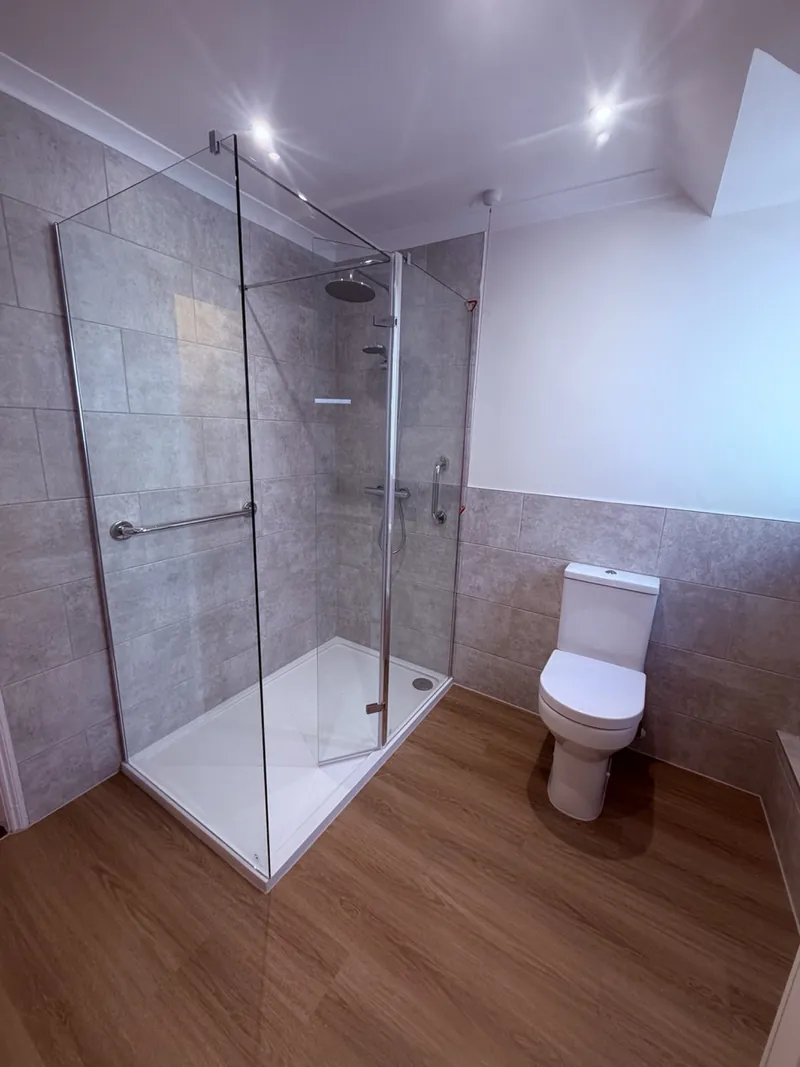 Walk-in shower with a low, wide tray, glass panels and grab rails