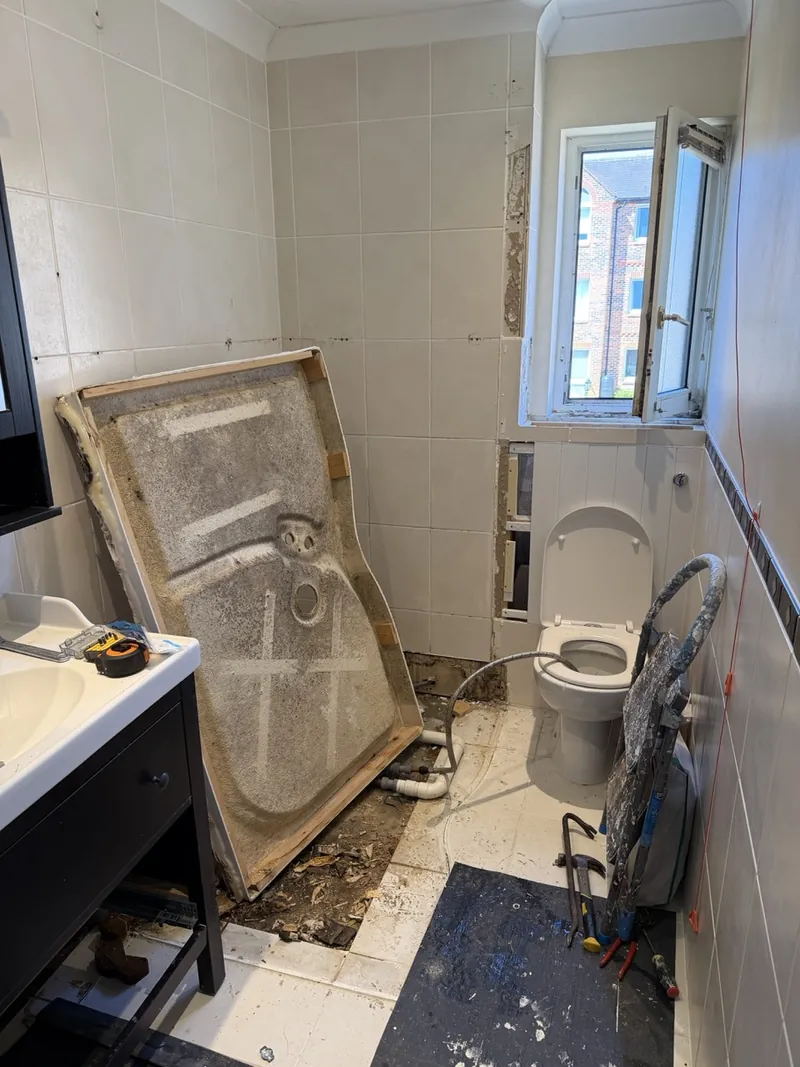 An old bathroom partly stripped out, with the shower tray lifted